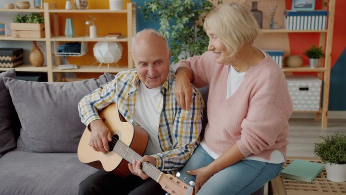 A senior couple playing guitar together at home